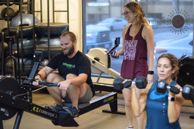 Personal trainer coaches two clients through rowing and strength exercises during a small-group training session at The Energy Lab in Redlands, CA.
